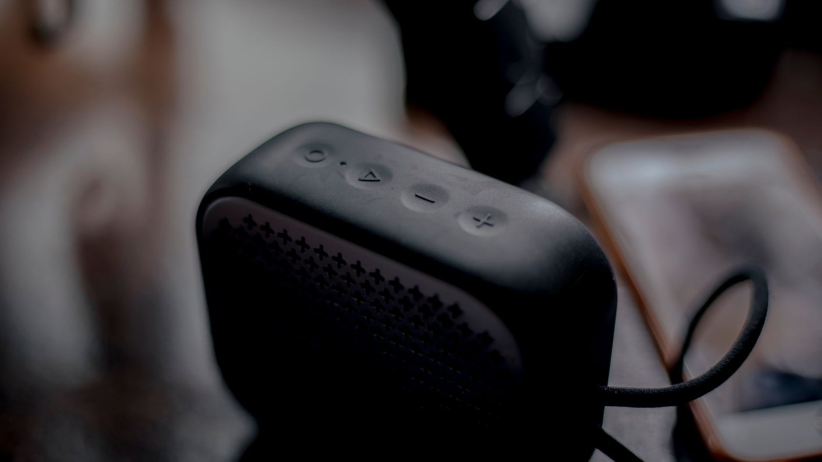 Caixa de som portátil Bluetooth compacta e moderna, em preto fosco, com controles táteis na parte superior e grade de som texturizada