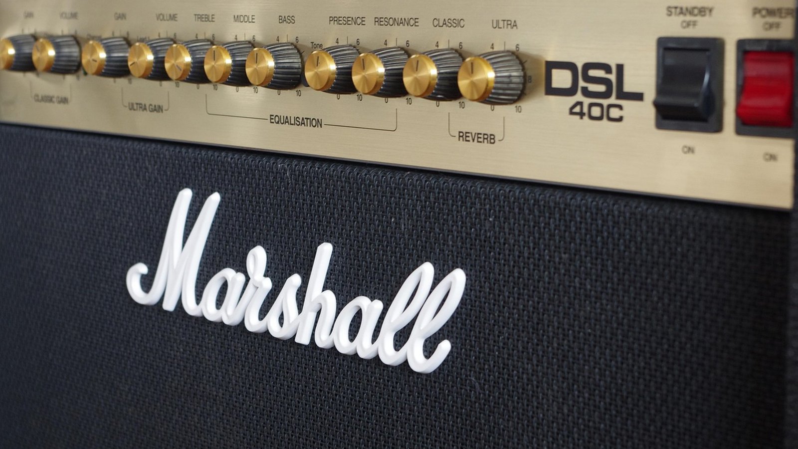 Amplificador valvulado Marshall DSL 40C com controles analógicos dourados e preto, logo 'Marshall' em branco sobre tela de tecido