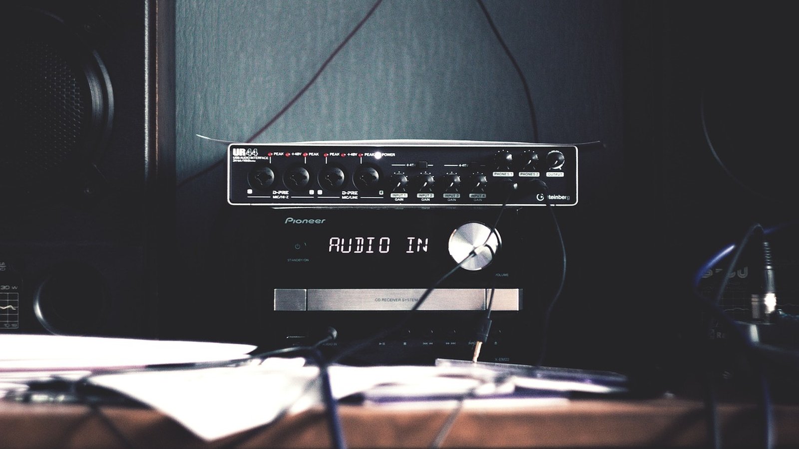 Equipamento de som hi-fi ativo: amplificador integrado Pioneer com pré-amplificador/amp de entrada (modelos como URE-414 ou similar) e conexões de áudio, em ambiente de estúdio com fios, papel e alto-
