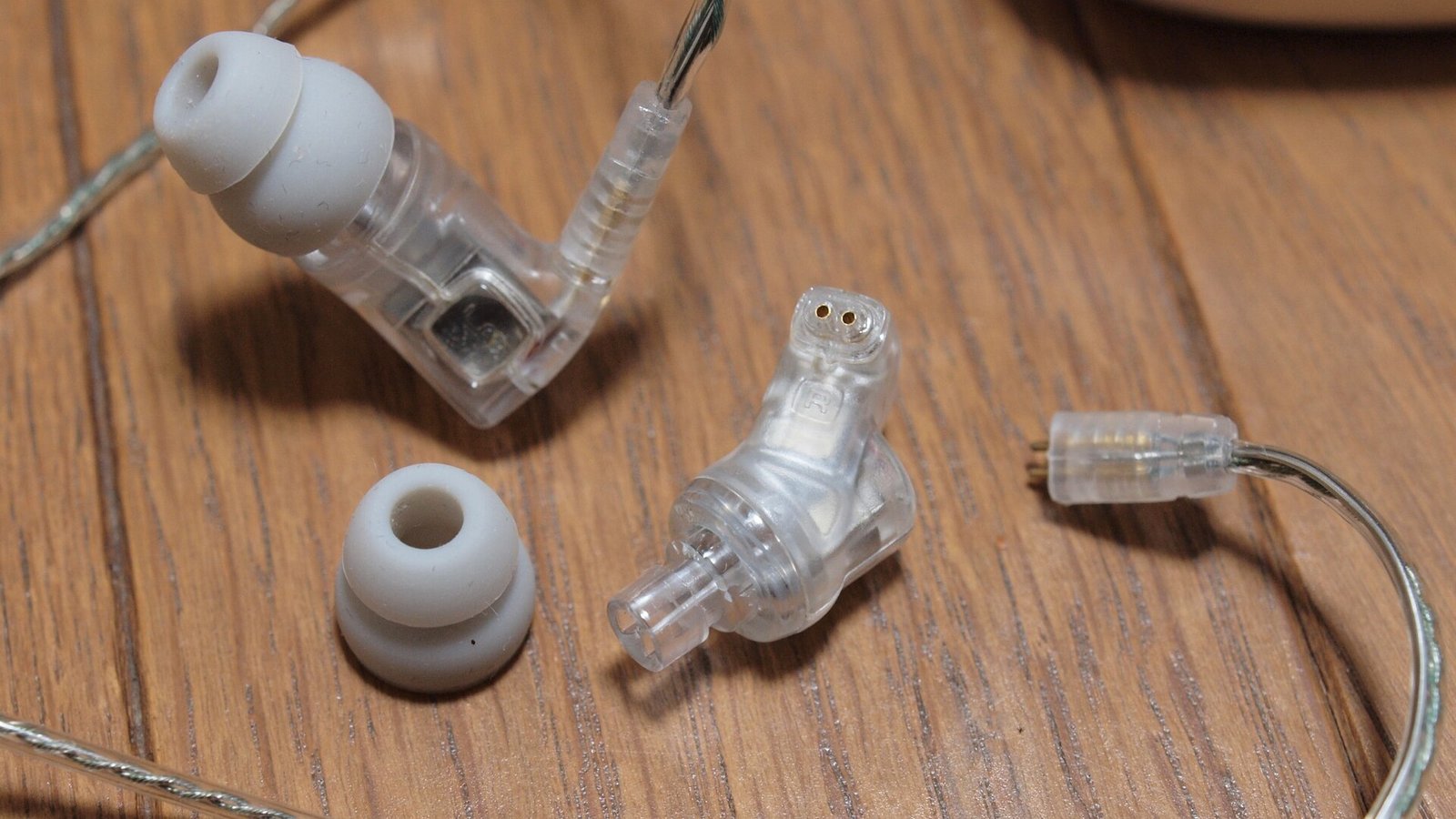História da Ultimate Ears: fone de ouvido in-ear transparente da Ultimate Ears, com almofadas de silicone cinza e fio metálico, disposto sobre superfície de madeira