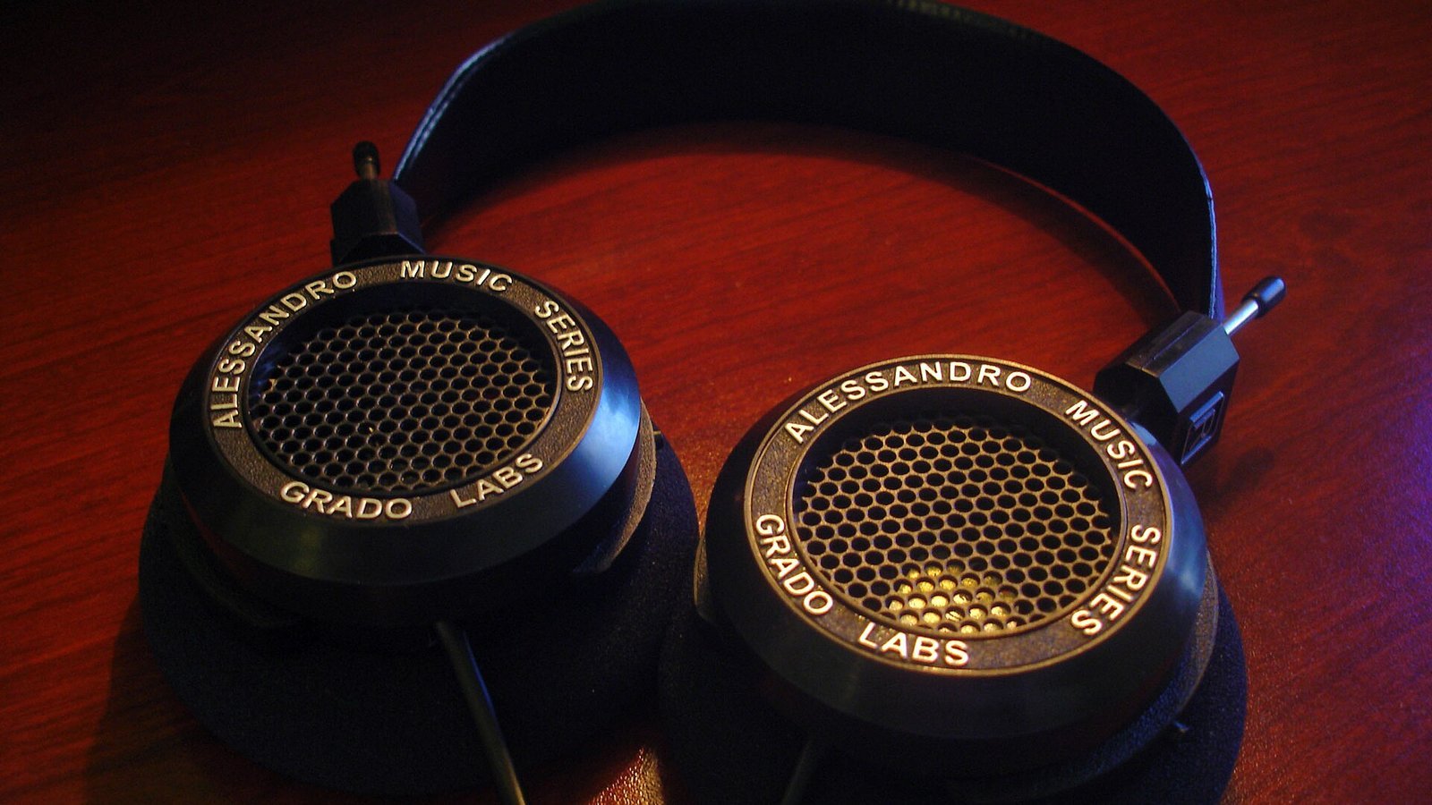 História da Grado Labs: fones de ouvido Grado Labs Alessandro Music Series, modelo com grade hexagonal e logotipo dourado, sobre superfície de madeira escura, iluminação quente e foco nítido no produt