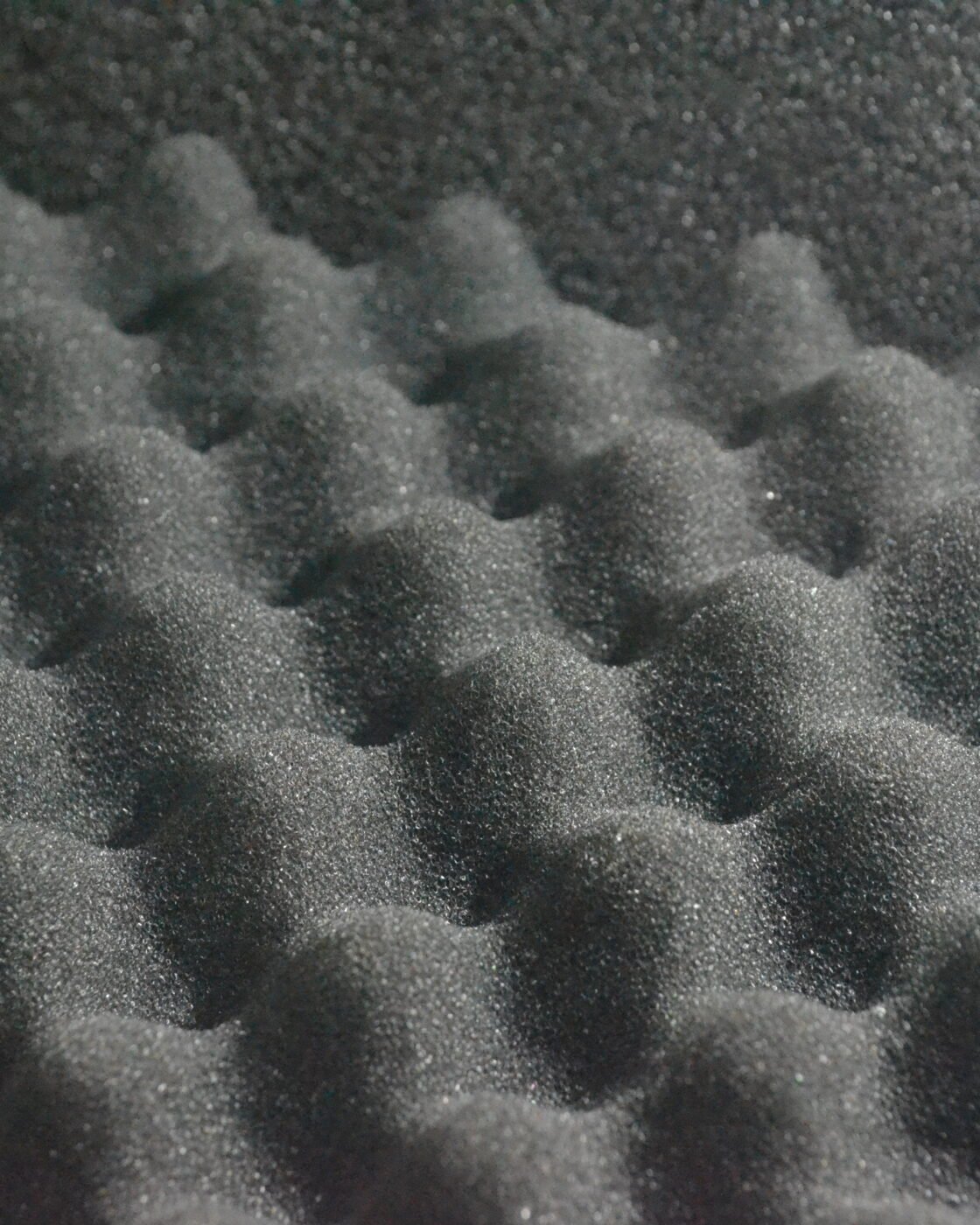 Close-up de espuma acústica cinza em formato de cunhas, material que absorve reflexões mas não isola o som entre cômodos
