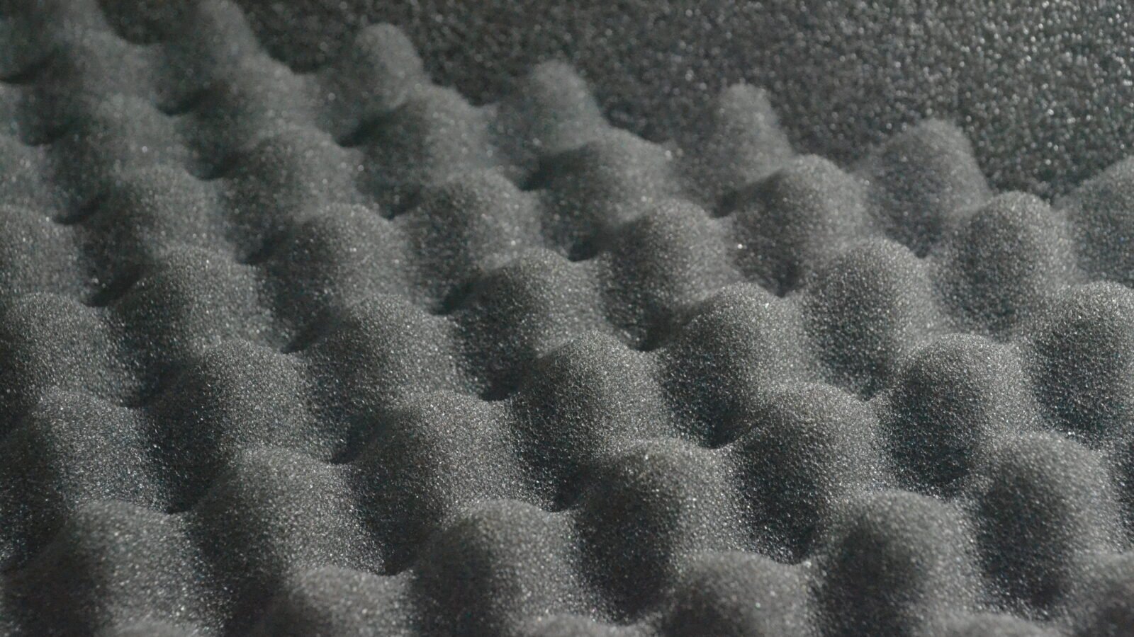 Close-up de espuma acústica cinza em formato de cunhas, material que absorve reflexões mas não isola o som entre cômodos