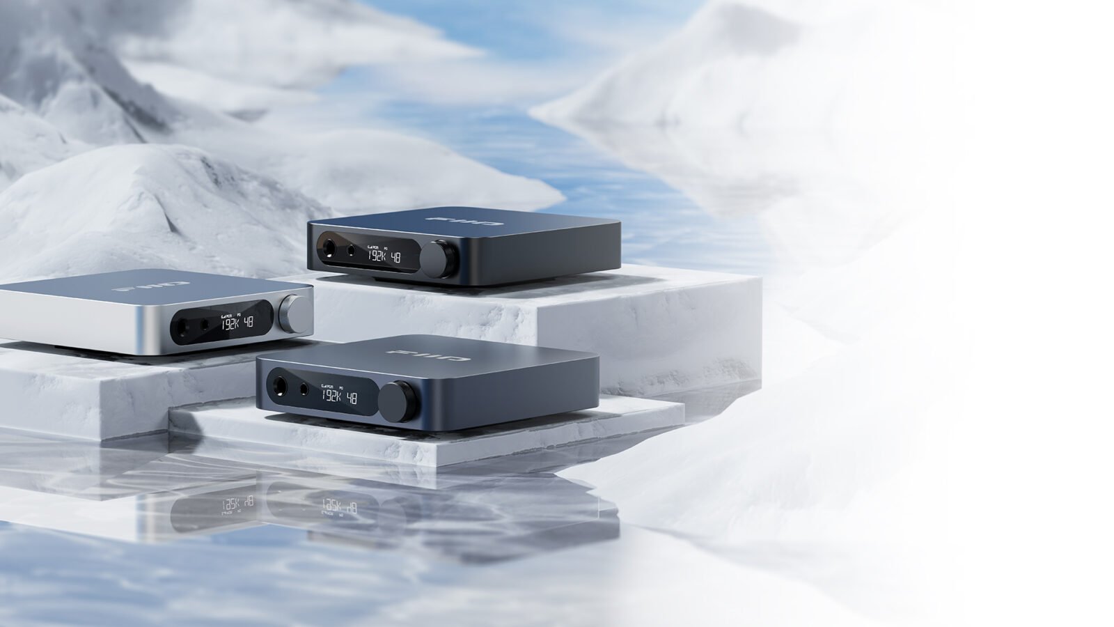 Três unidades do DAC/amplificador de mesa FiiO K11 nas cores preta, prata e titânio sobre blocos brancos