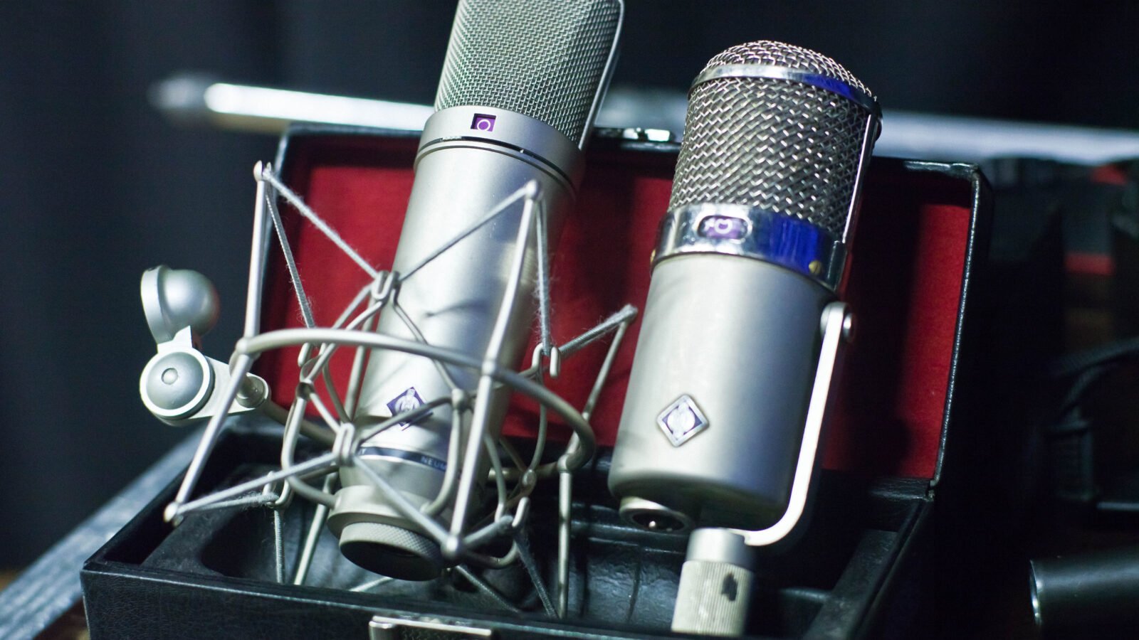 Microfones condensadores Neumann U 87 e U 47 montados lado a lado em pedestais em um estúdio de gravação