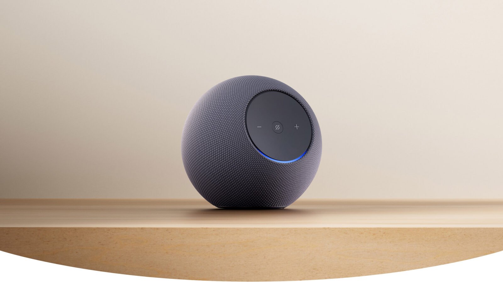Amazon Echo Studio 2025 na cor grafite, com formato esférico e anel de luz azul, sobre prateleira de madeira