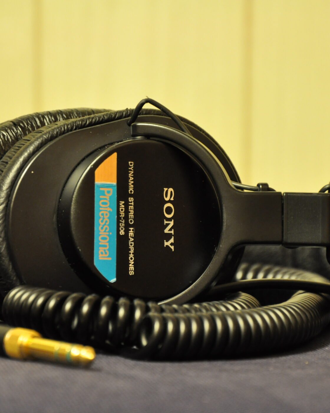 Fone de ouvido Sony MDR-7506 dobrado sobre uma mesa, com cabo espiralado e plugue dourado com adaptador P10