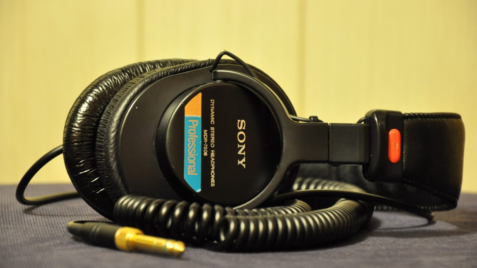 Fone de ouvido Sony MDR-7506 dobrado sobre uma mesa, com cabo espiralado e plugue dourado com adaptador P10