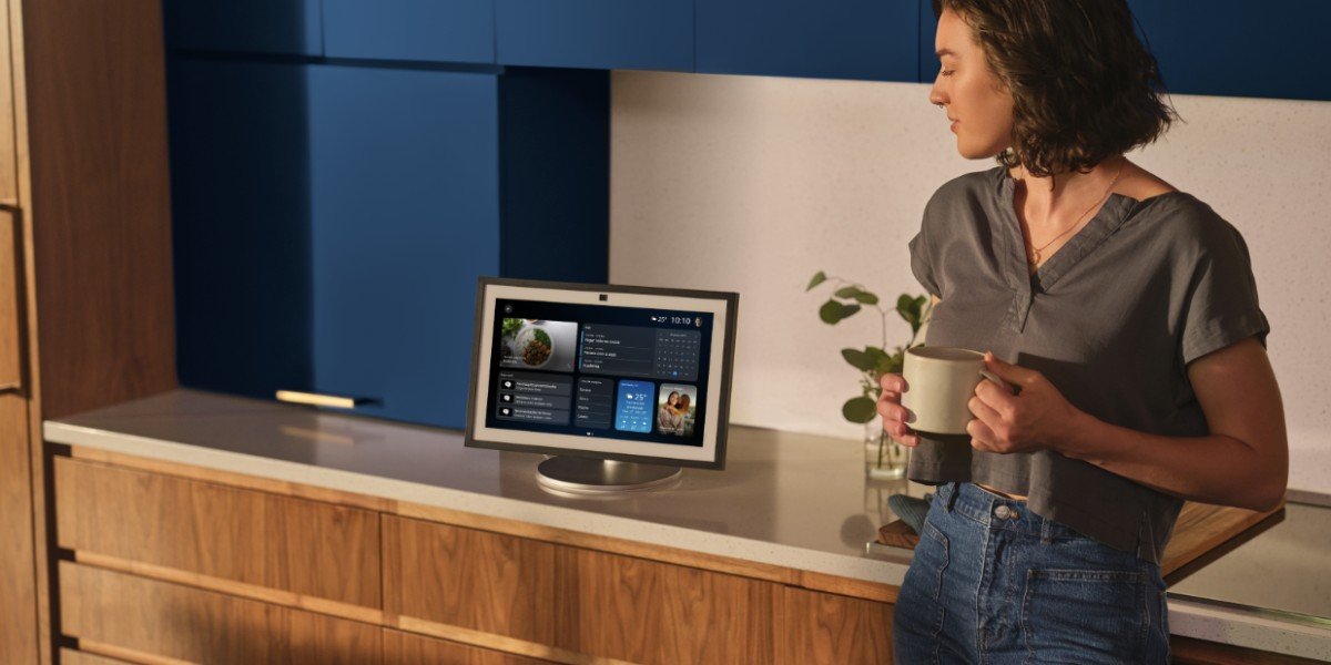 Mulher segurando uma caneca ao lado de um Amazon Echo Show com a tela inicial da Alexa+, em imagem oficial de lançamento da Amazon Brasil