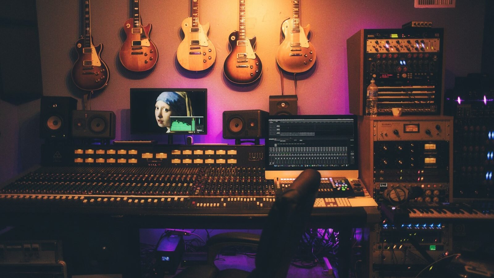 Sala de controle de estúdio com monitores de referência, mesa de som e guitarras na parede