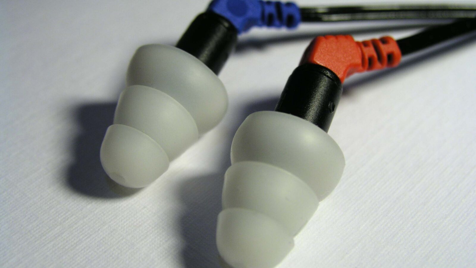 Fones in-ear com ponteiras de silicone de três abas (triple flange) sobre superfície branca