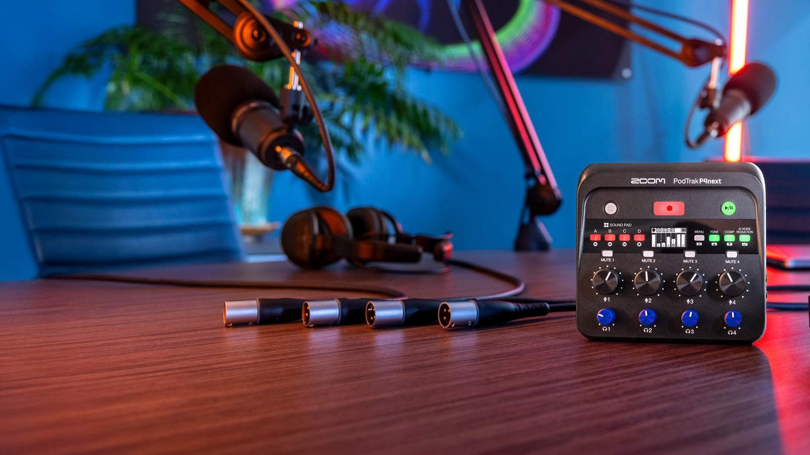 Gravador de podcast Zoom PodTrak P4next sobre a mesa, com quatro cabos XLR, fones de ouvido e dois microfones em braços articulados