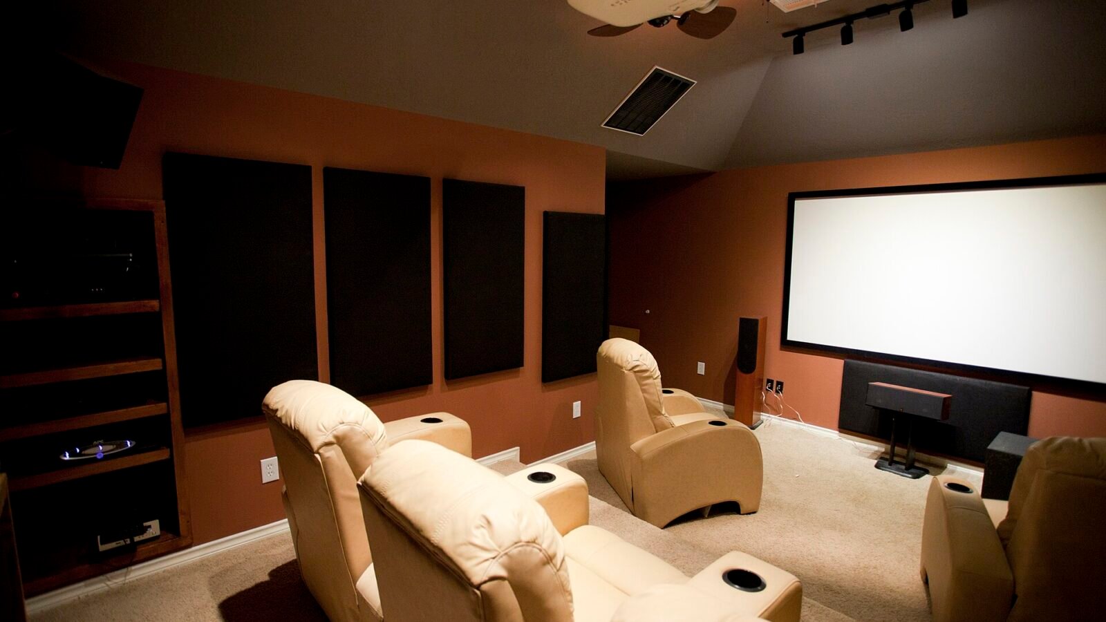 Sala de home theater dedicada com painéis acústicos na parede lateral, tela de projeção, projetor no teto e poltronas reclináveis