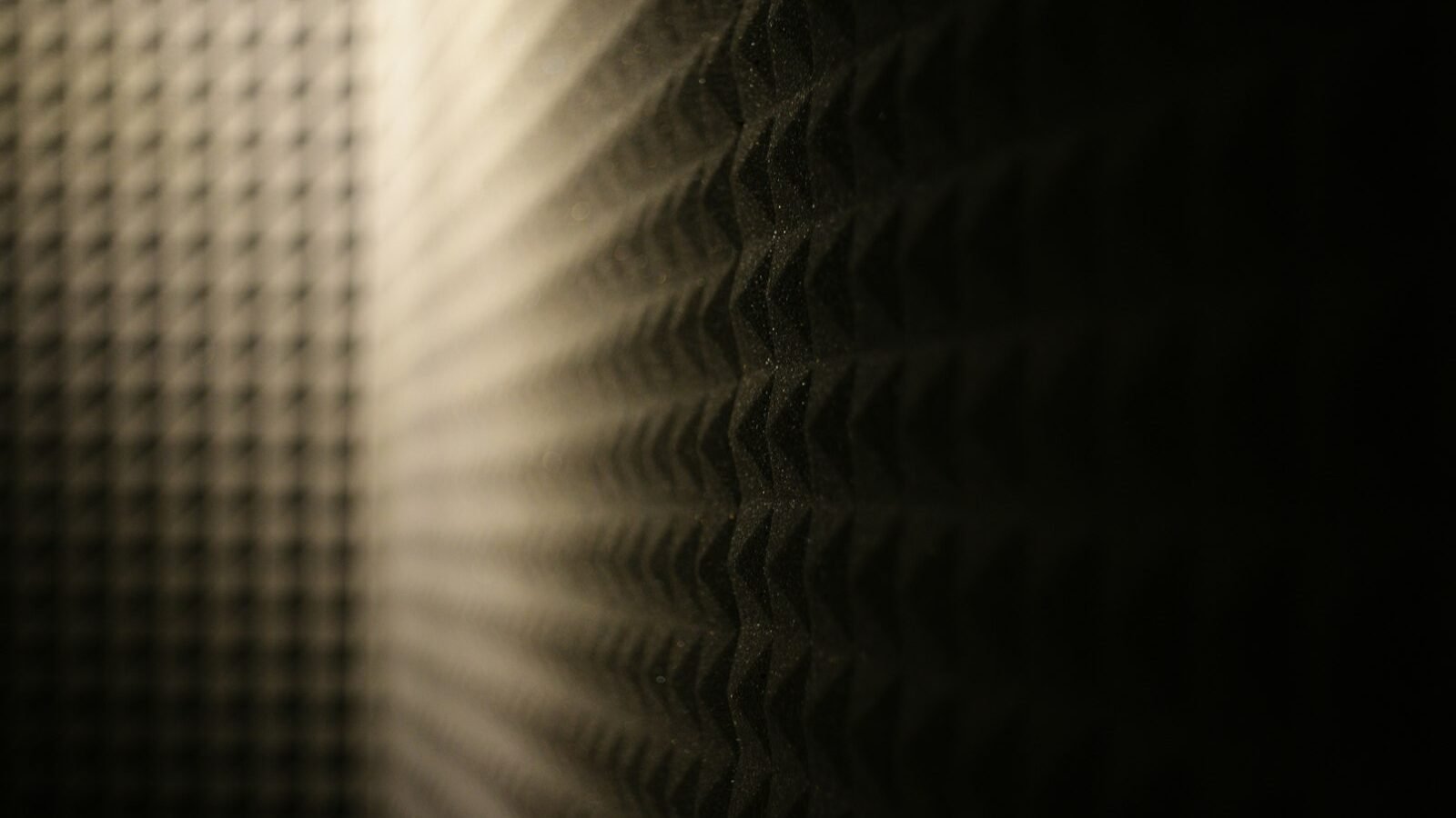 Close de espuma acústica com relevo piramidal em parede, iluminada lateralmente