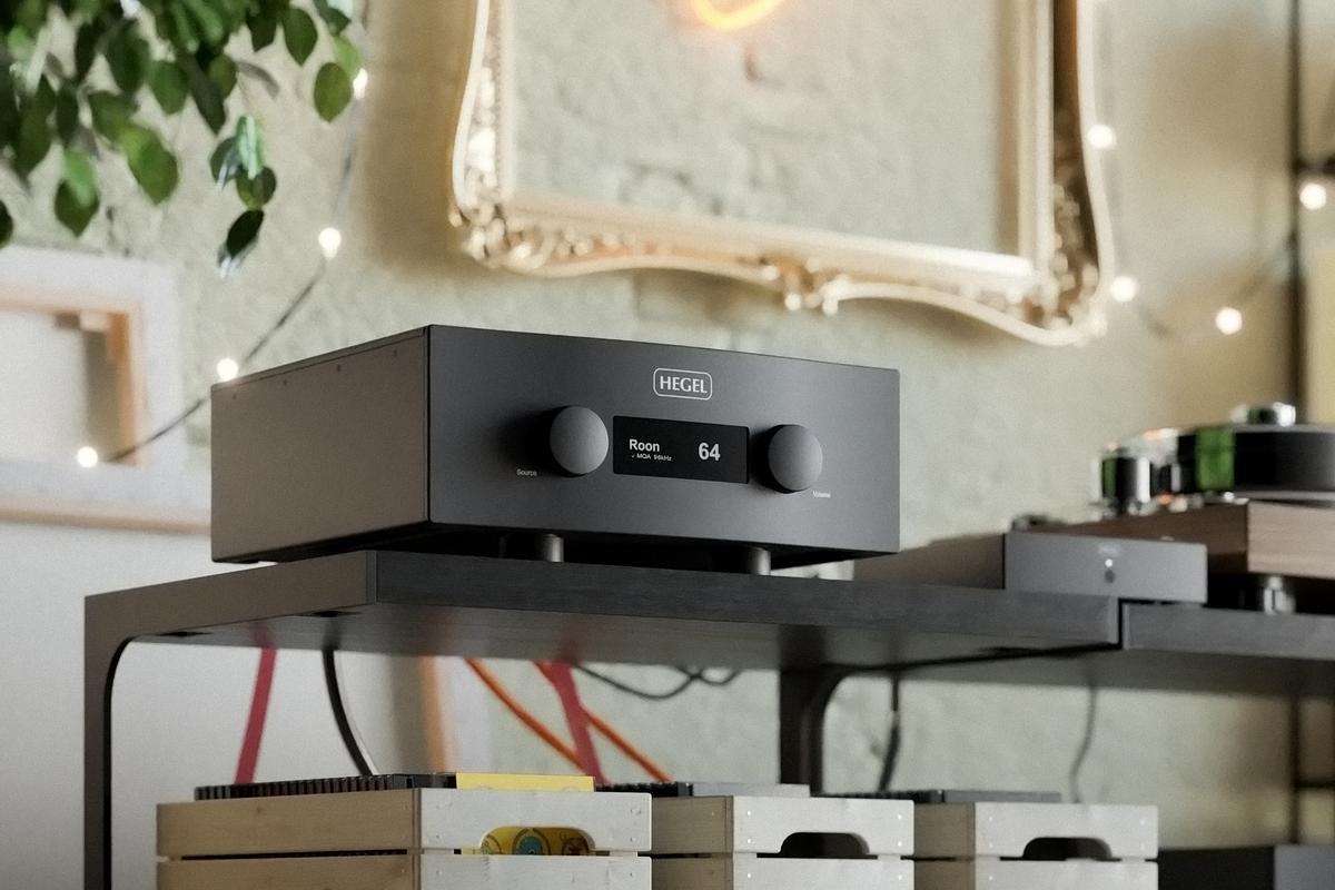 Amplificador integrado Hegel H600 preto sobre um rack, com display mostrando Roon e volume 64