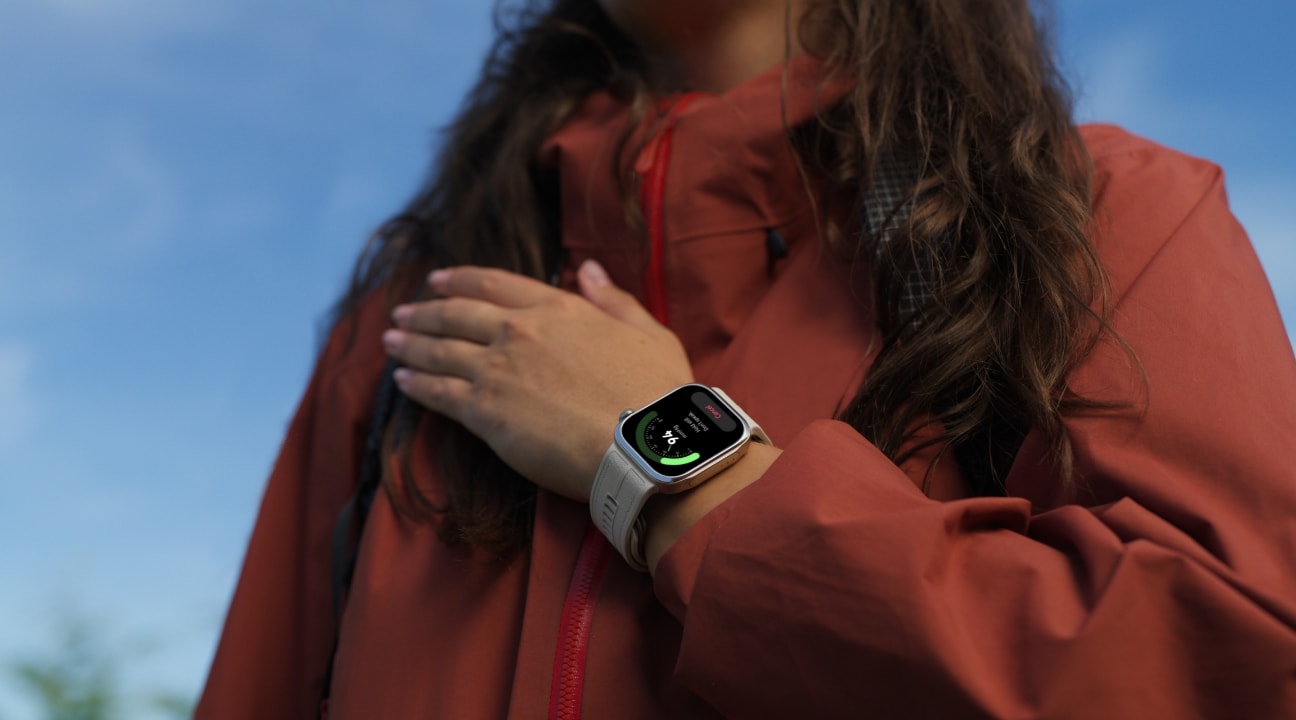 Mulher de jaqueta vermelha com o smartwatch Huawei Watch D3 de pulseira branca no pulso, mostrando na tela uma medição de saúde, com céu azul ao fundo