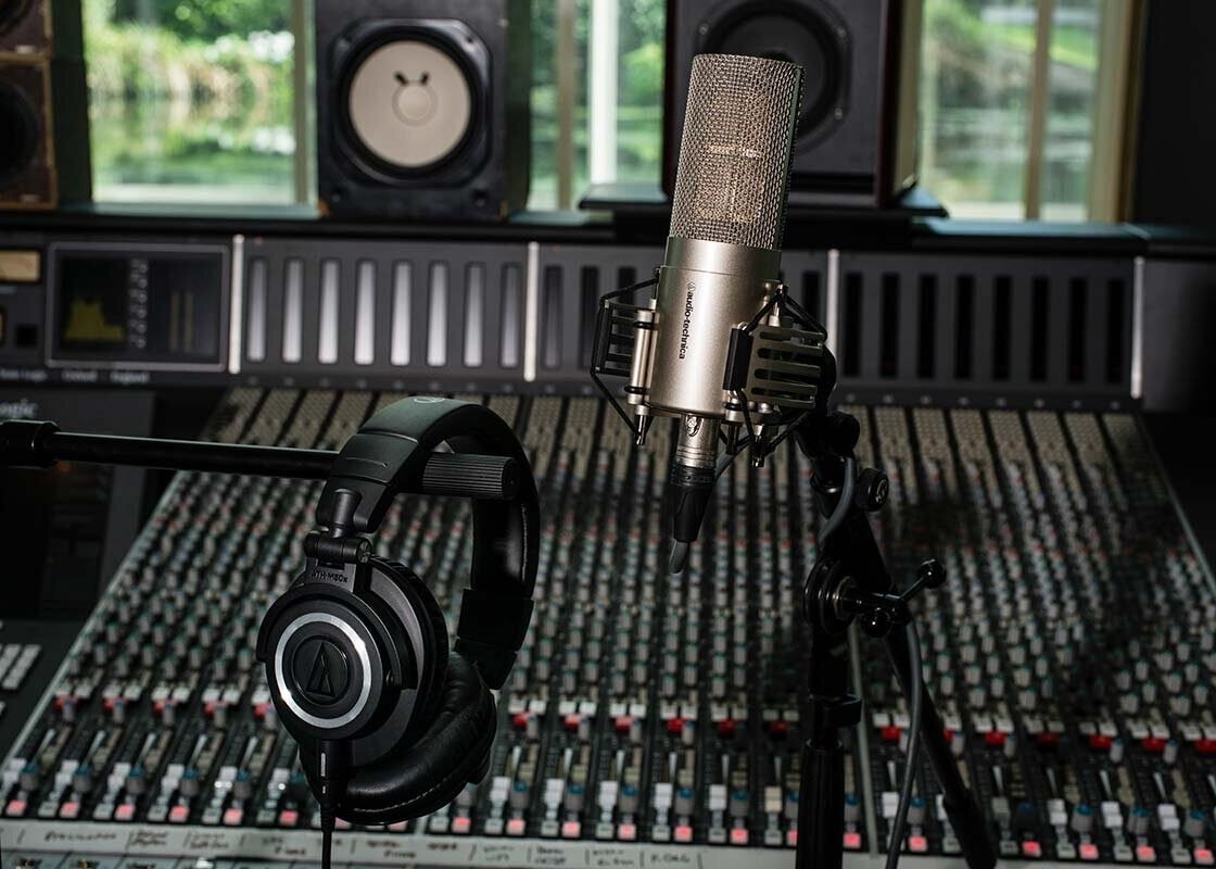 Fone de estúdio fechado Audio-Technica ATH-M50x apoiado em pedestal diante de uma mesa de som