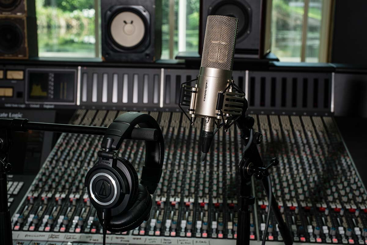 Fone de estúdio fechado Audio-Technica ATH-M50x apoiado em pedestal diante de uma mesa de som