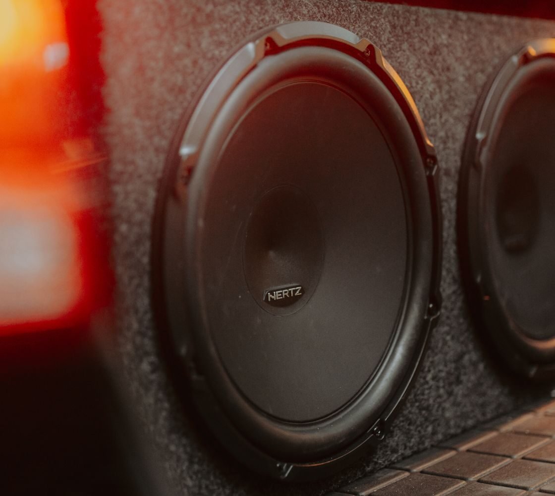 Caixa de subwoofer com dois alto-falantes de 12 polegadas instalada no porta-malas de um carro, iluminada pelas lanternas traseiras