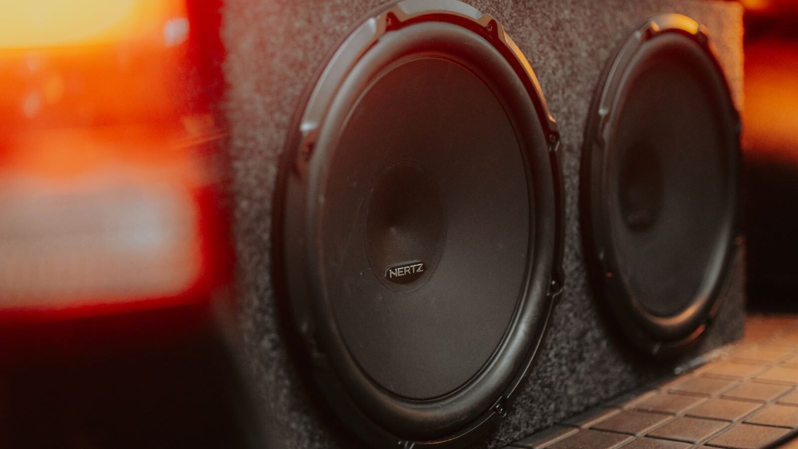 Caixa de subwoofer com dois alto-falantes de 12 polegadas instalada no porta-malas de um carro, iluminada pelas lanternas traseiras