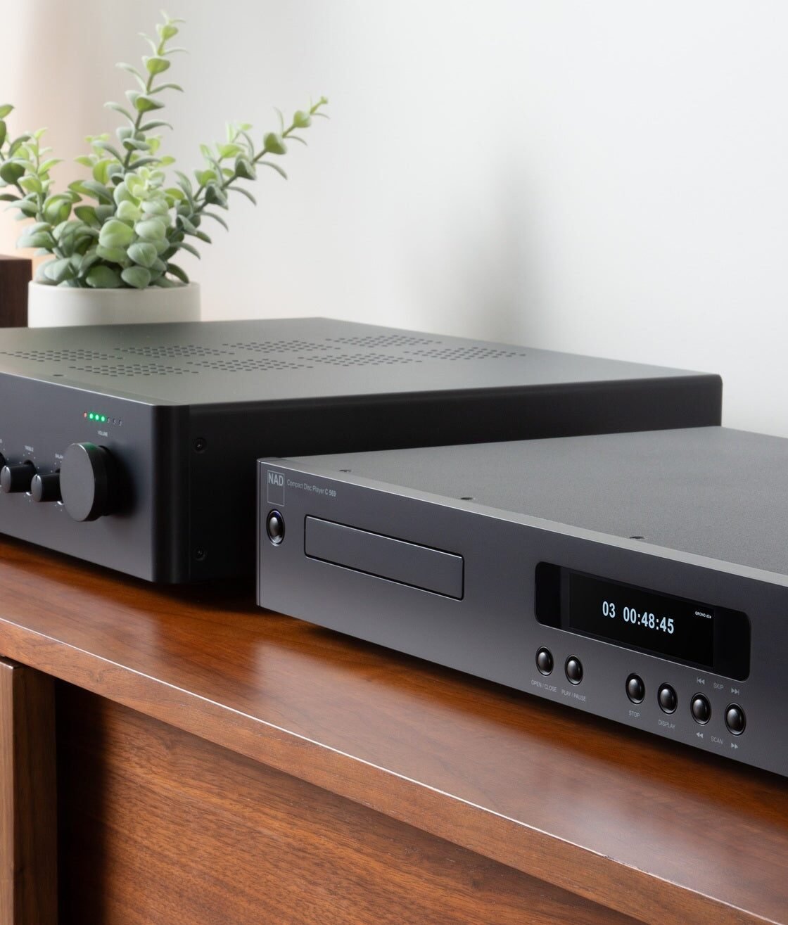 Amplificador integrado NAD C 359S e CD player NAD C 569 empilhados sobre um aparador, em foto oficial da NAD