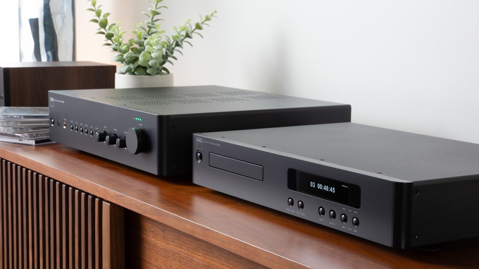 Amplificador integrado NAD C 359S e CD player NAD C 569 empilhados sobre um aparador, em foto oficial da NAD