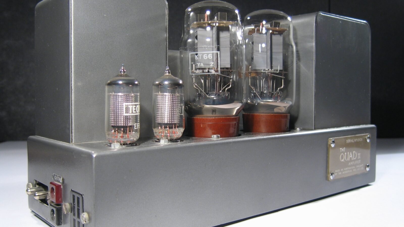 Amplificador valvulado Quad II, com duas válvulas KT66, duas EF86 e transformadores em gabinete cinza, fotografado sobre fundo escuro