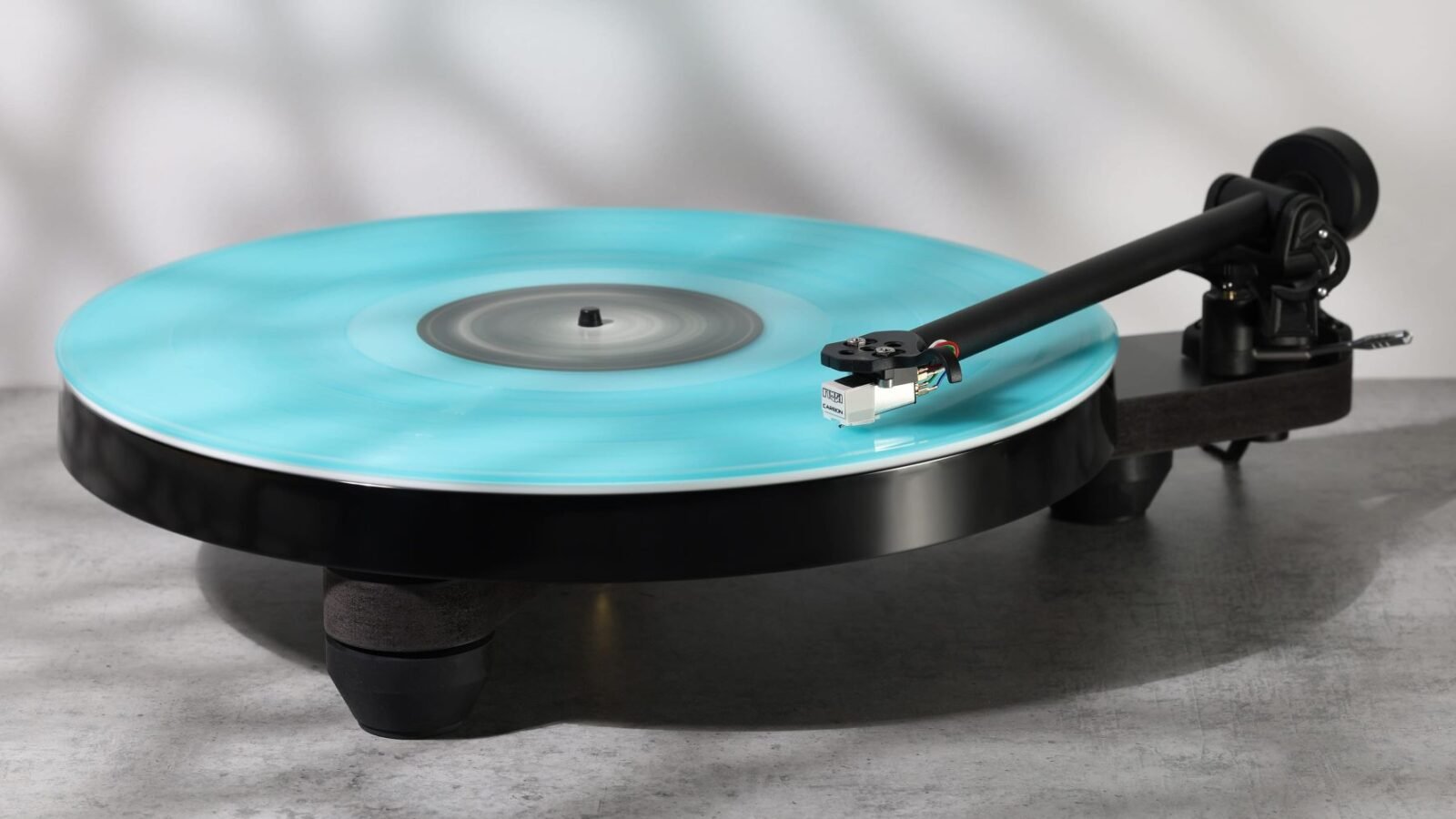 Toca-discos Rega Replay com plinto esqueletal preto, braço RB110 e cápsula Carbon tocando um disco de vinil azul