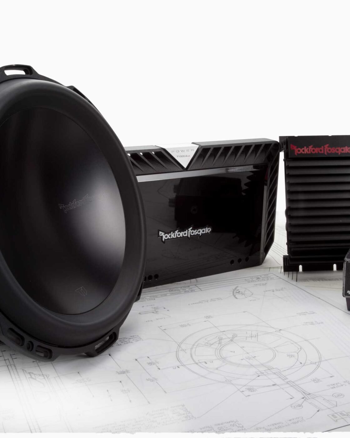 Produtos Rockford Fosgate de várias épocas sobre plantas técnicas: um subwoofer, um amplificador moderno, um amplificador Punch 45HD e um antigo equalizador Fosgate PowerPunch