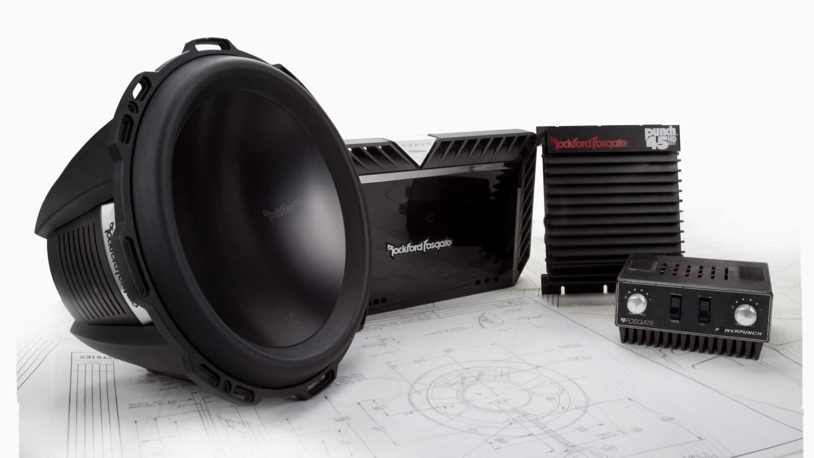 Produtos Rockford Fosgate de várias épocas sobre plantas técnicas: um subwoofer, um amplificador moderno, um amplificador Punch 45HD e um antigo equalizador Fosgate PowerPunch