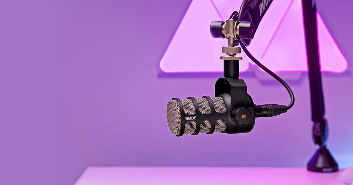 Microfone dinâmico RØDE PodMic preto preso a braço articulado, em fundo roxo
