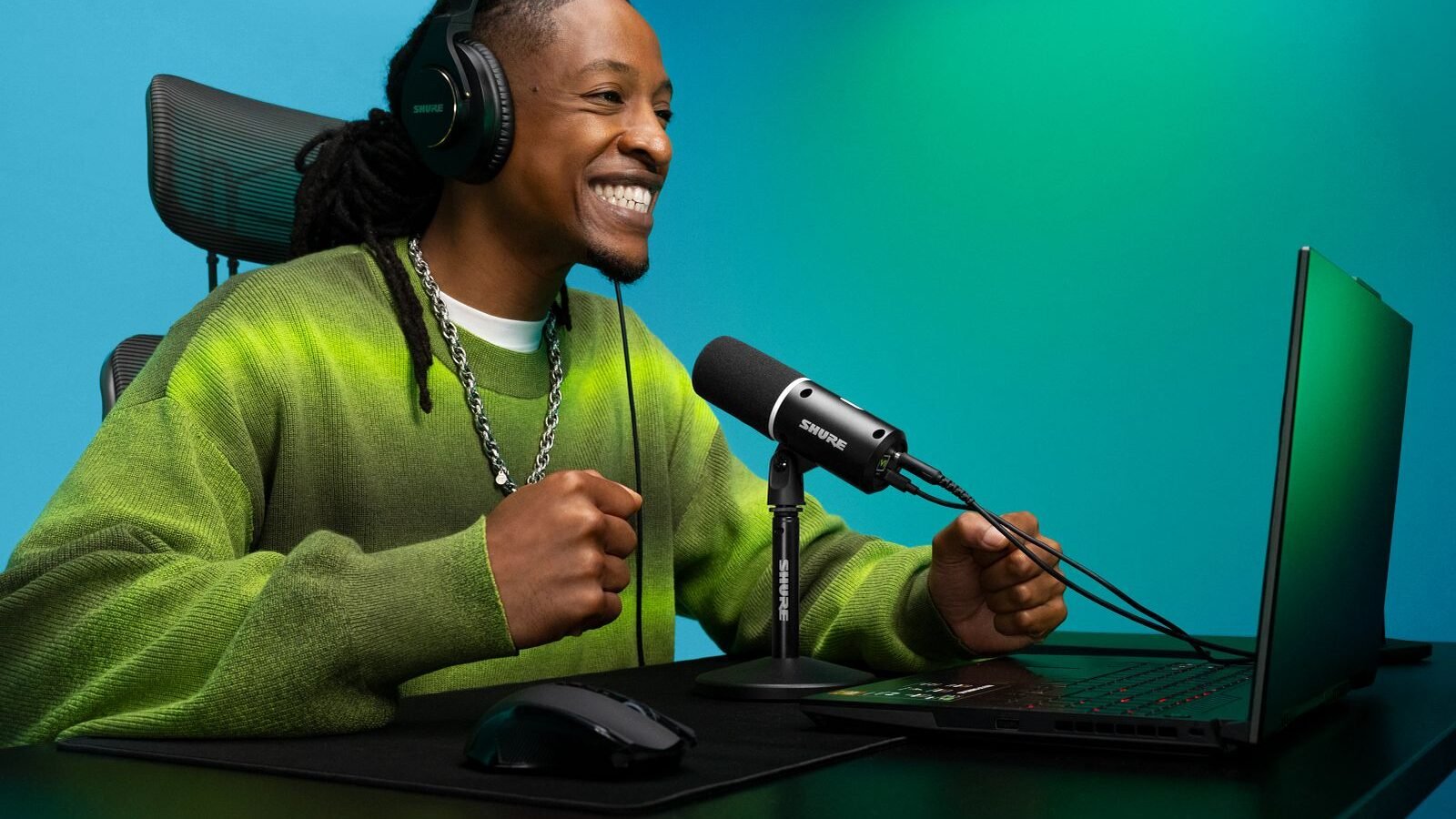 Microfone Shure MV6 Gen 2 preto em seu suporte de mesa, ao lado de um notebook