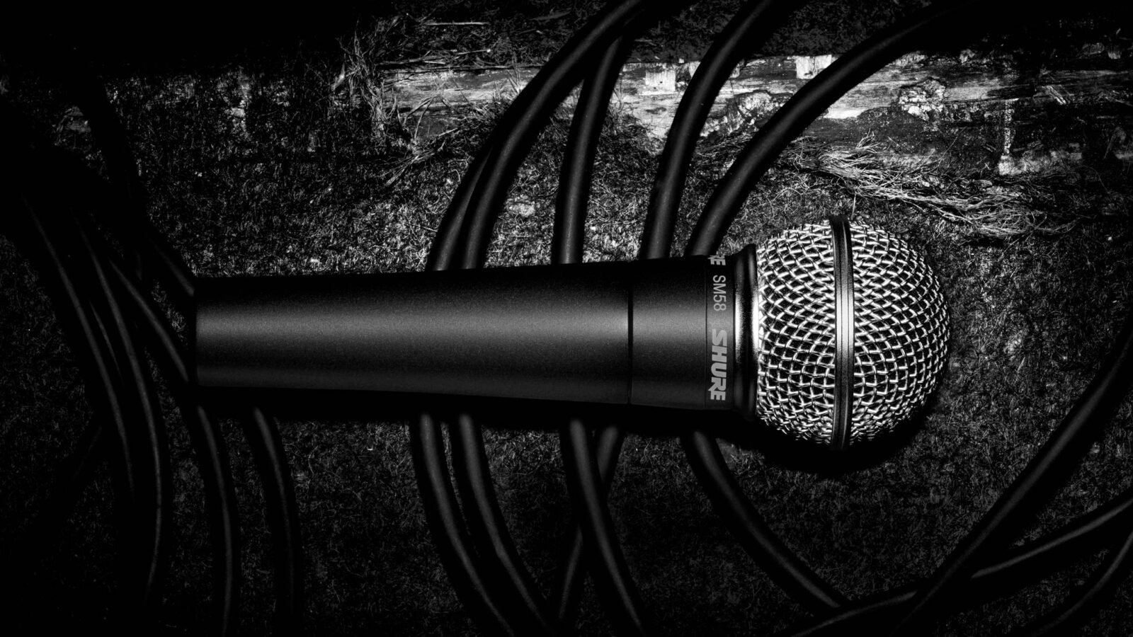 Microfone Shure SM58 com grelha prateada sobre fundo escuro, com cabos ao redor
