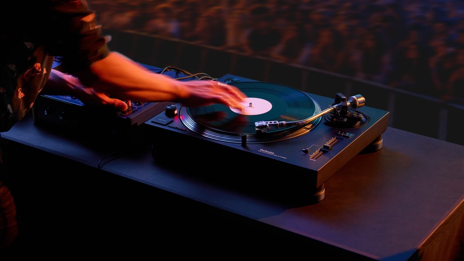Toca-discos Technics SL-1210MKX preto com braço prateado em cabine de DJ