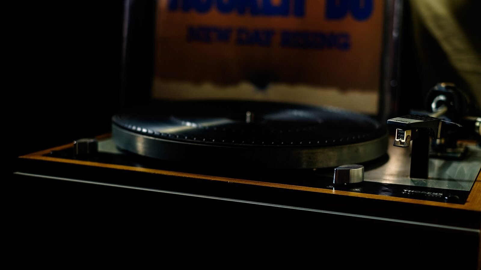 Toca-discos Thorens TD 160 com plinto de madeira, braço com cápsula e disco de vinil no prato, fotografado em ambiente escuro