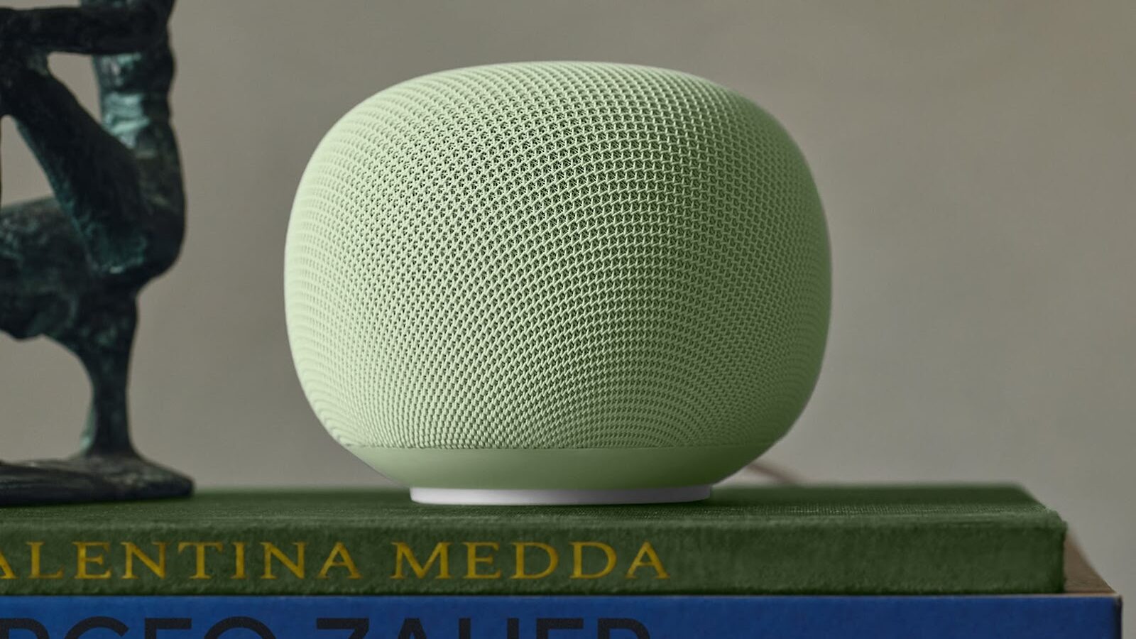 Alto-falante do Google Home redondo, com tecido verde claro, apoiado sobre livros numa estante